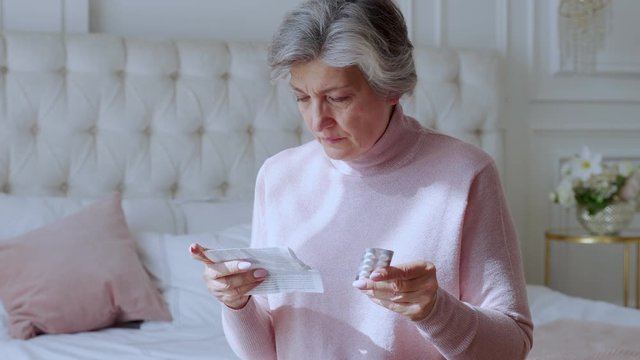 An elderly woman with tablets in her hands and reads a prescription medication.