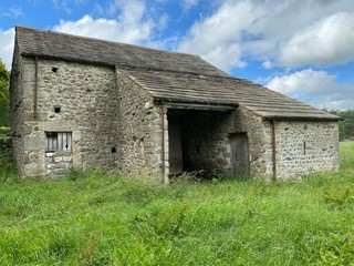 Fototapeta na wymiar Old barn, with a stone slate roof, in an uncut field, on a cloudy day in, Malham, Skipton, UK