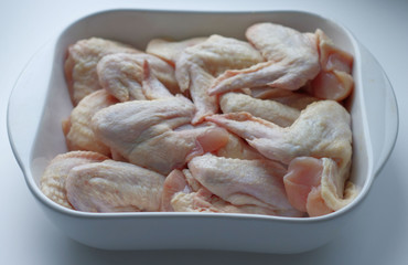 Fototapeta na wymiar Chicken wings with skin in a white glass plate. Ingredients, fresh, cut meat for cooking. Chicken parts, protein. Diet meat