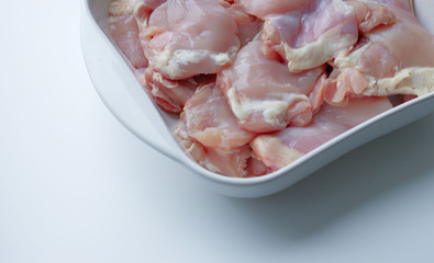 Chicken thigh fillet with skin, in a white glass plate, on a gray background. Ingredients, fresh, cut meat for cooking. Chicken parts, protein. Diet meat, fillet in a plate