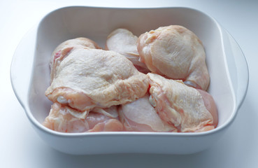chicken thighs with skin, in a white glass plate, on a gray background. Ingredients, fresh, sliced meat for cooking. Chicken parts, protein. Diet meat, fillet in a plate. Place for text