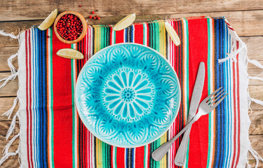 Festive Mexican table setting. Plate and cutlery with colorful napkin on rustic wooden background....