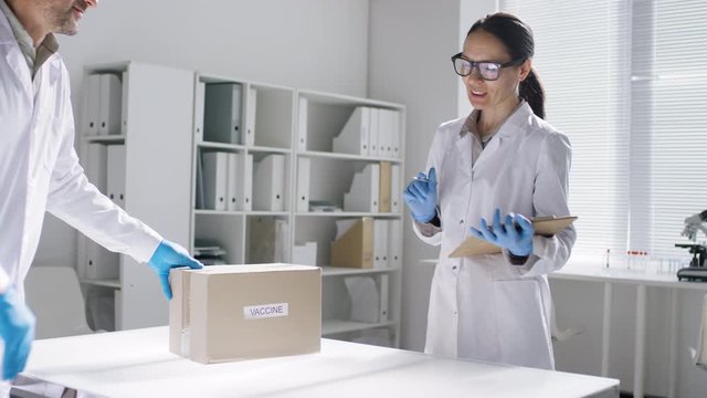Sequence of shots of female doctor in lab coat recieving box of covid-19 vaccines, then filling syringe from ampule and squirting it