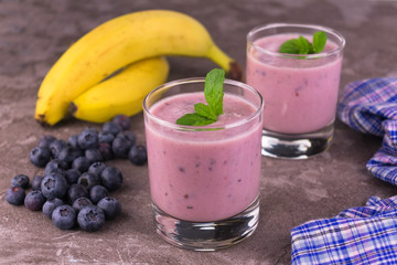 Blueberry banana smoothie in a transparent glass on a gray background.