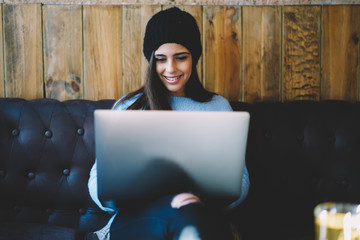Smiling copywriter in trendy hat watching interesting webinar on modern laptop device.Cheerful...