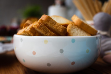 Wheat flour mini toast in a clay bowl, birthday party background. Square croutons in a white bowl on a wooden table. Side view. Close-up. Selective focus.