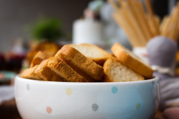 Wheat flour mini toast in a clay bowl, birthday party background. Square croutons in a white bowl on a wooden table. Side view. Close-up. Selective focus.