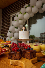 First anniversary party. Chocolate cake with berries on a wooden plate. Delicious desserts on rustic wooden table with the anniversary cake in the background. Diversity of pastry decorated with fruit.
