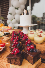 First anniversary party. Chocolate cake with berries on a wooden plate. Delicious desserts on rustic wooden table with the anniversary cake in the background. Diversity of pastry decorated with fruit.