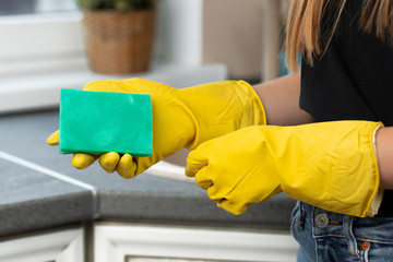 Hands of a woman in yellow gloves holding green sponge