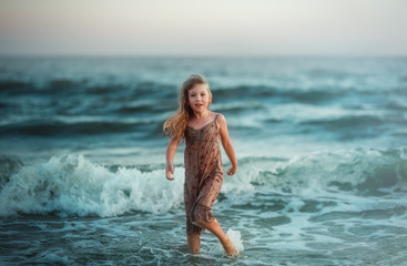 a girl with her hair down and in a wet sundress stands in a choppy sea with waves and smiles