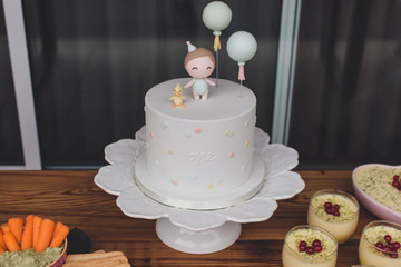 First Anniversary party. A beautiful first birthday stylish white cake decorated with balloons, a little boy figure and his cute duckling. The concept of festive desserts.