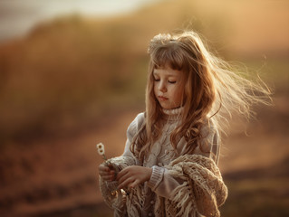 
a girl with loose hair stands in the wind in a warm sweater and looks at the daisies in her hands