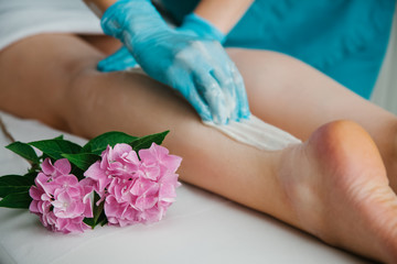 Obraz na płótnie Canvas A bunch of flowers next to feet on the white background. Pure leg skin concept. Wax Epilation concep. Sugaring master putting epilation wax paste on the legs.