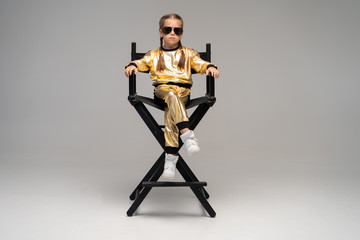 a little girl in gold suit sits on a chair. Isolated on a yellow background