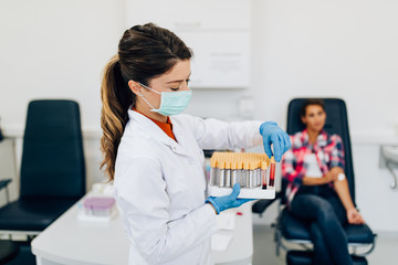 Nurse taking blood sample from young female patient in the background. Selective focus on sample tube.