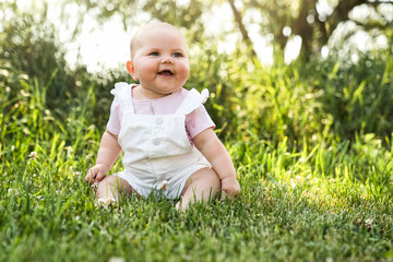 Happy adorable chubby baby girl sitting on the grass