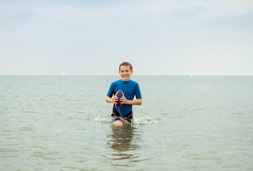 Portrait of handsome teen boy playing with ball in neoprene swimsuit in sea