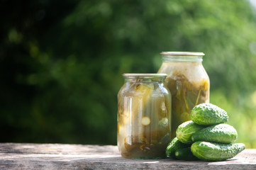 Pickled cucumbers, jars of pickled and fresh cucumbers on a natural background, space for text