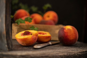 Fresh rose with yellow peaches, one of them sliced with knife on a wooden chair. In the middle with a bone, on a black background. Selective focus with copy space.