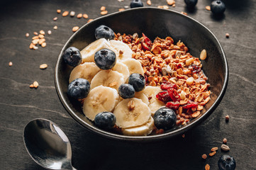 Healthy breakfast concept with homemade granola with banana and blueberries on black wooden background