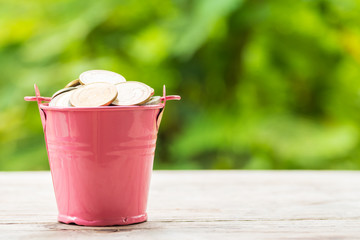 Pink aluminum bucket overflowing with coins over wooden table