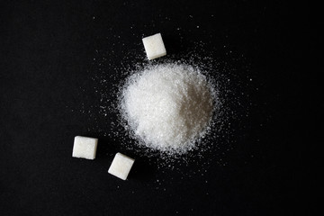 Scattered sugar in a pile and refined sugar cubes on a black background