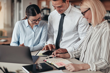 Smiling businesspeople looking at something on a colleague's cel