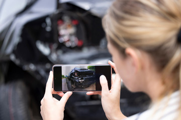 Female Driver Taking Photo Of Damaged Car After Accident For Insurance Claim On Mobile Phone