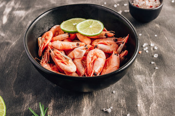 Top view of bowl with boiled shrimps with lime in black bowl on dark background.