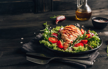 Grilled chicken fillet and fresh vegetable salad of tomatoes and arugula leaves. Healthy food. Black background.