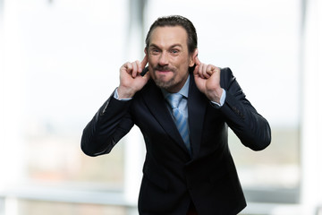 Mature businessman making monkey face. Caucasian man in business suit grimacing and teasing someone on blurred background.