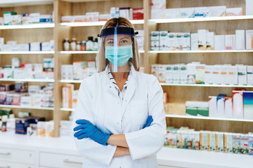 Female pharmacist with protective mask on her face talking on phone while working at pharmacy. Medical healthcare concept.