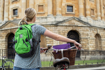 Rear View Of Female Student Riding Old Fashioned Bicycle Around Oxford University College Buildings...