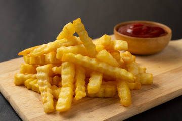 Tasty french fries with ketchup on cutting board, on the black table background