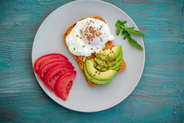Toast with poached egg, flaxseeds, avocado and tomato slices, arugula leaves on a plate. Healthy meal for breakfast.