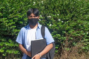 Latino college boy with face mask holding books