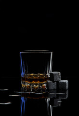 
Glass with whiskey and granite cubes on black glass table