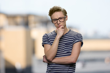 Pensive guy wearing eyeglasses touching chin.Thoughtful nerd boy on abstract blurred background....
