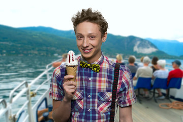 Cheerful teen boy holding cone ice cream. Abstract blurred mountains and sea in the background. Vacation and tourism concept.