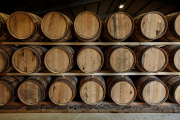 A front on view of a row of stacks of traditional full whisky barrels, set down to mature, in a large warehouse
