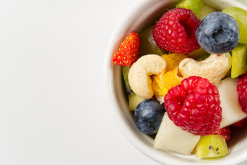 Bowl of healthy fresh fruit salad on white background, top view copy space.