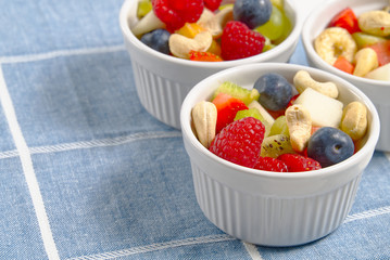 Bowl of healthy fresh fruit salad on linen blue towel background, top view copy space.