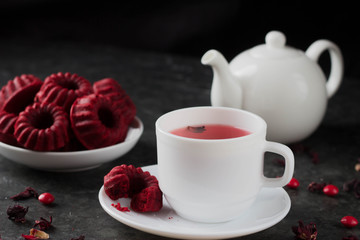 Red tea in a white mug and red cupcakes with rings on a white plate and a teapot