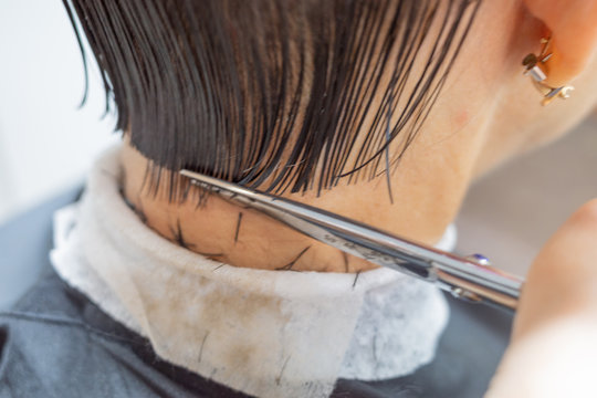 Image of hairdresser hand cuts client hair with scissors. Hairdresser cuts woman hair