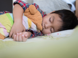 Asian child boy sleeping on bed in bed room. Young kid hugging favorite teddy bear and taking a nap...