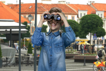 Boy observing city using binoculars. Curious child in denim jacket exploring the city. Tourism and...