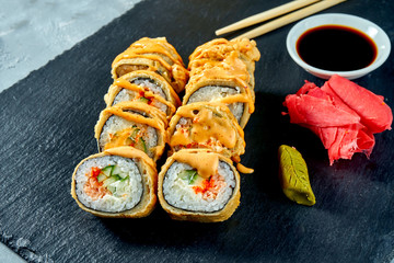 Deep fried sushi rolls with salmon and cucumber in tempura on a black slate board. Selective focus Selective focus