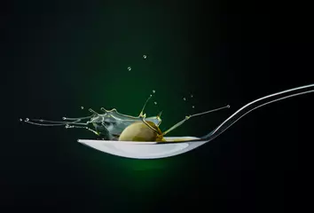 Küchenrückwand glas motiv closeup of green olive with splashing oil on a spoon on a dark background © vitaly tiagunov