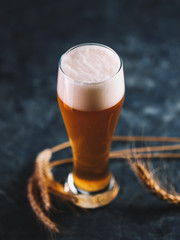A glass of unfiltered foamy beer on a dark table